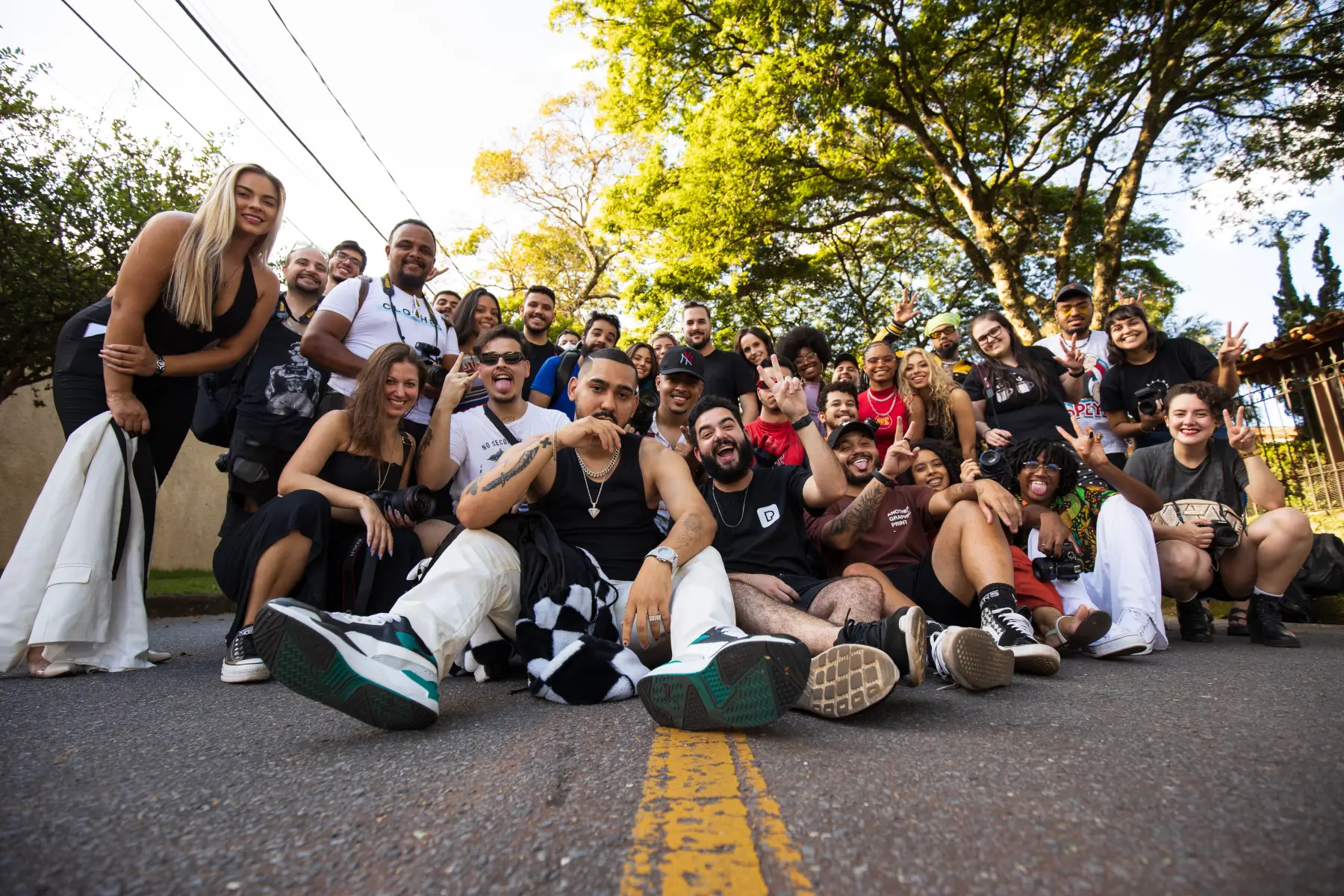 A big group of smiling people posed close together for a photo on a tree-lined street
